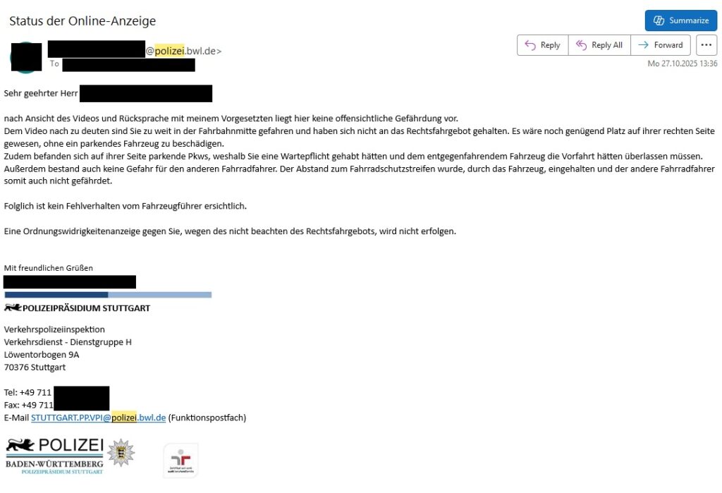 Das Bild zeigt eine E-Mail der Polizei, die über den Status einer Online-Anzeige informiert und mitteilt, dass keine Ordnungswidrigkeit vorliegt. Es handelt sich um eine E-Mail mit dem Betreff "Status der Online-Anzeige". Die E-Mail ist an eine Person gerichtet, deren Name und E-Mail-Adresse unkenntlich gemacht sind. Der Absender ist die Polizei Baden-Württemberg, genauer gesagt die Polizeipräsidium Stuttgart, Verkehrspolizeiinspektion, Dienstgruppe H. Die E-Mail datiert vom 27. Oktober 2025, 13:36 Uhr. Inhaltlich informiert die E-Mail den Empfänger, dass nach Sichtung eines Videos und Rücksprache mit einem Vorgesetzten keine offensichtliche Gefährdung vorliegt. Es wird erklärt, dass das Video zeigt, wie der Empfänger nicht genau auf der rechten Fahrbahnseite fuhr, aber ausreichend Platz auf der rechten Seite war, um eine Gefährdung zu vermeiden. Auch gegenüber entgegenkommenden Fahrzeugen und anderen Fahrradfahrern wurde keine Gefahr verursacht. Daher wird keine Ordnungswidrigkeitenanzeige wegen Nichtbeachtens des Rechtsfahrgebots erfolgen. Die E-Mail enthält die üblichen Elemente eines offiziellen Schreibens: Anrede ("Sehr geehrter Herr"), Grußformel ("Mit freundlichen Grüßen"), Kontaktdaten (Telefon, Fax, E-Mail) und ein Logo der Polizei Baden-Württemberg. Die Atmosphäre ist formell und sachlich, die Stimmung ist beruhigend, da keine Sanktionen zu erwarten sind. Die Farben sind überwiegend weiß (Hintergrund), schwarz (Text) und blau (Akzente, Logos). Die Komposition ist typisch für eine E-Mail-Ansicht in einem E-Mail-Client.